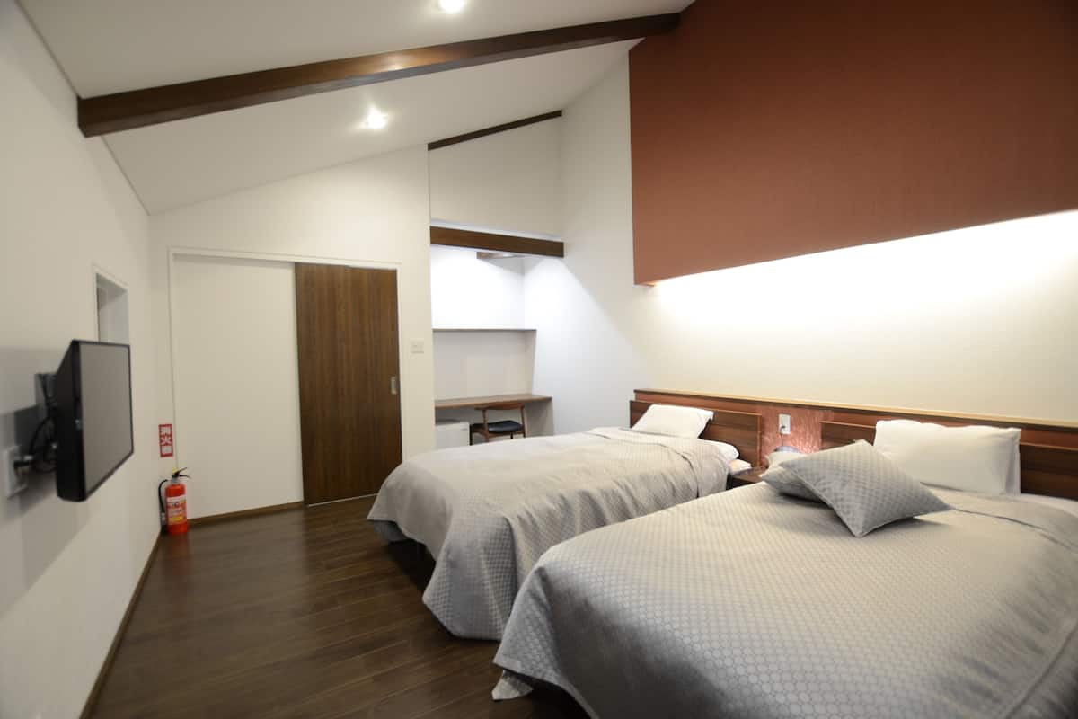 Habitación de hotel con dos camas, un televisor, un extintor y una viga de madera en el techo.