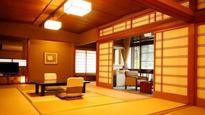 Um quarto com esteiras de tatame, televisão, sofá e uma porta tradicional japonesa deslizante.