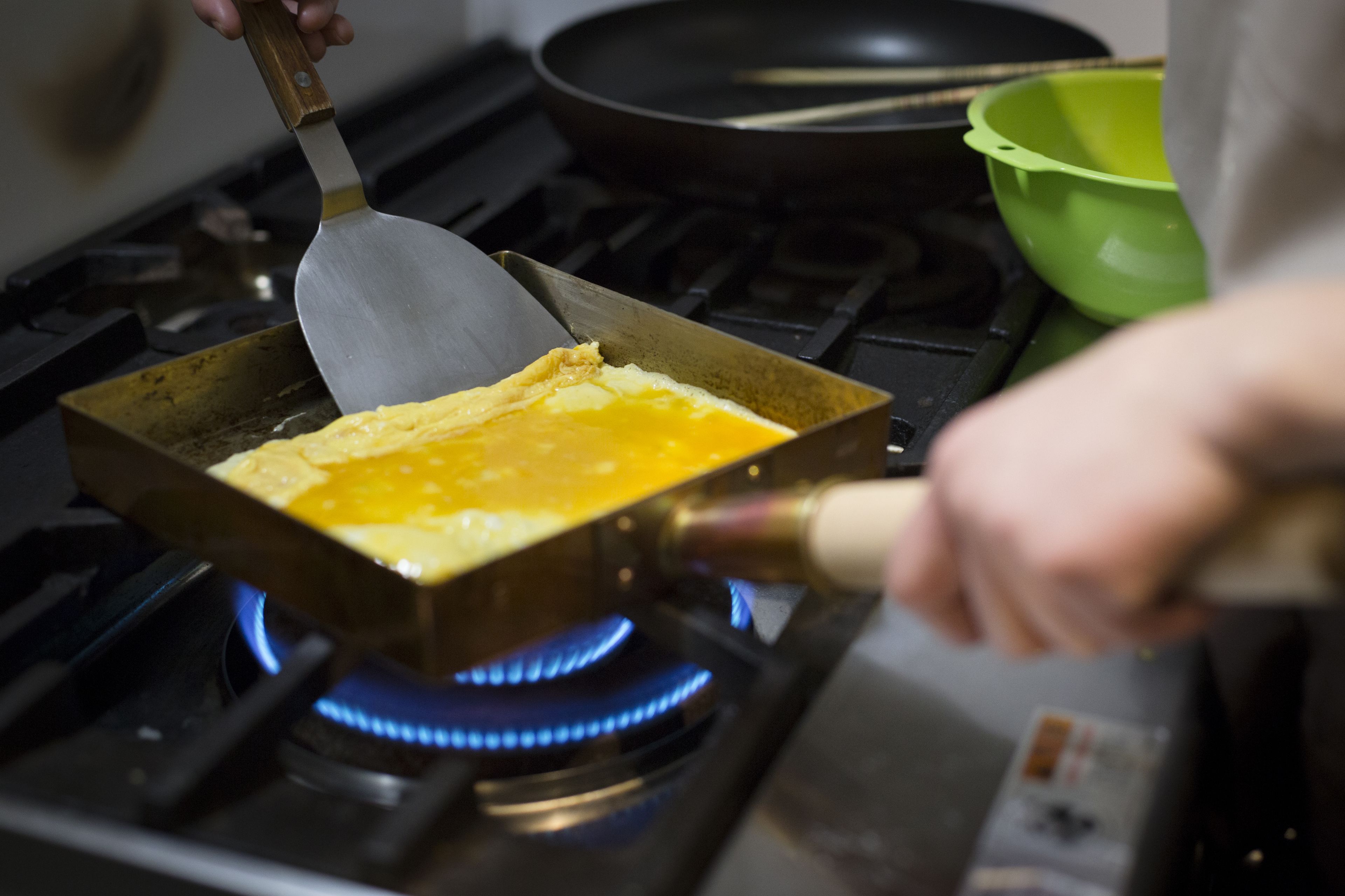 Une personne prépare une omelette dans une poêle sur une cuisinière à gaz.