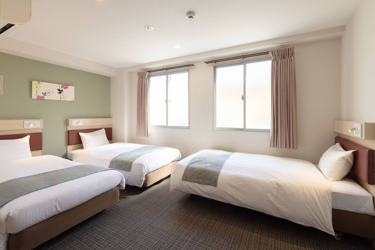 Ein Hotelzimmer mit zwei Einzelbetten, einem großen Fenster mit Vorhängen, einem an der Wand hängenden Kunstwerk und einem Teppichboden.