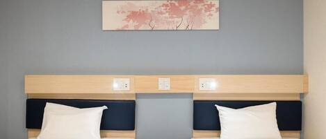 Habitación de hotel con diseño moderno, con dos camas con sábanas blancas, cabeceros de madera y una obra de arte en la pared que representa árboles.
