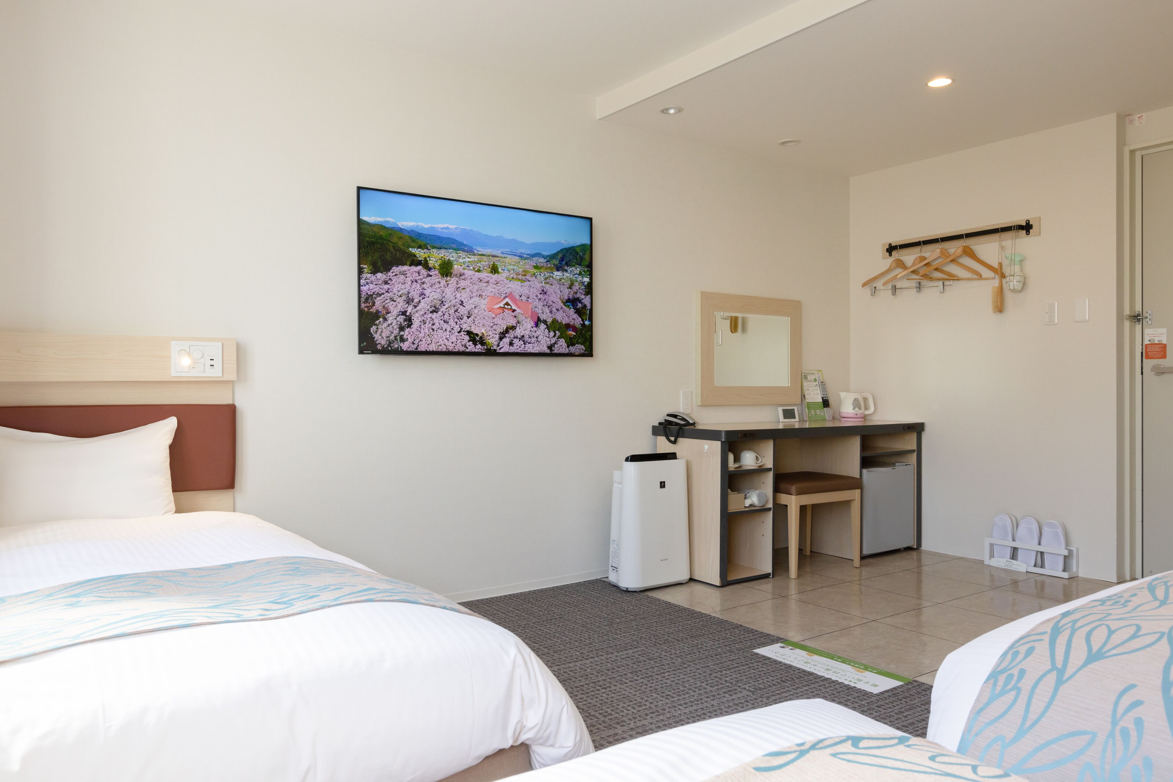 A hotel room with two beds, a desk, a small kitchenette, and a large window with a scenic view.