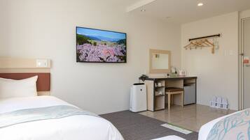 A hotel room with two beds, a desk, a small kitchenette, and a large window with a scenic view.