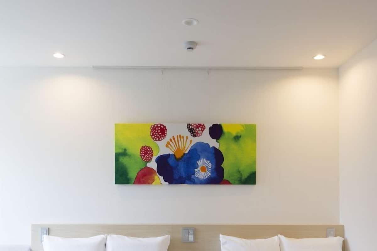Ein Hotelzimmer mit zwei Betten, einem Bild an der Wand und einer Deckenleuchte.