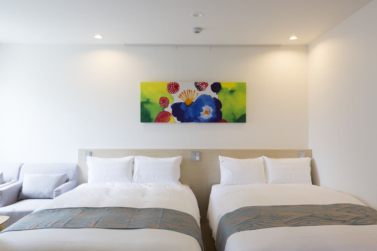 Ein Hotelzimmer mit zwei Betten, einem Bild an der Wand und einer Deckenleuchte.