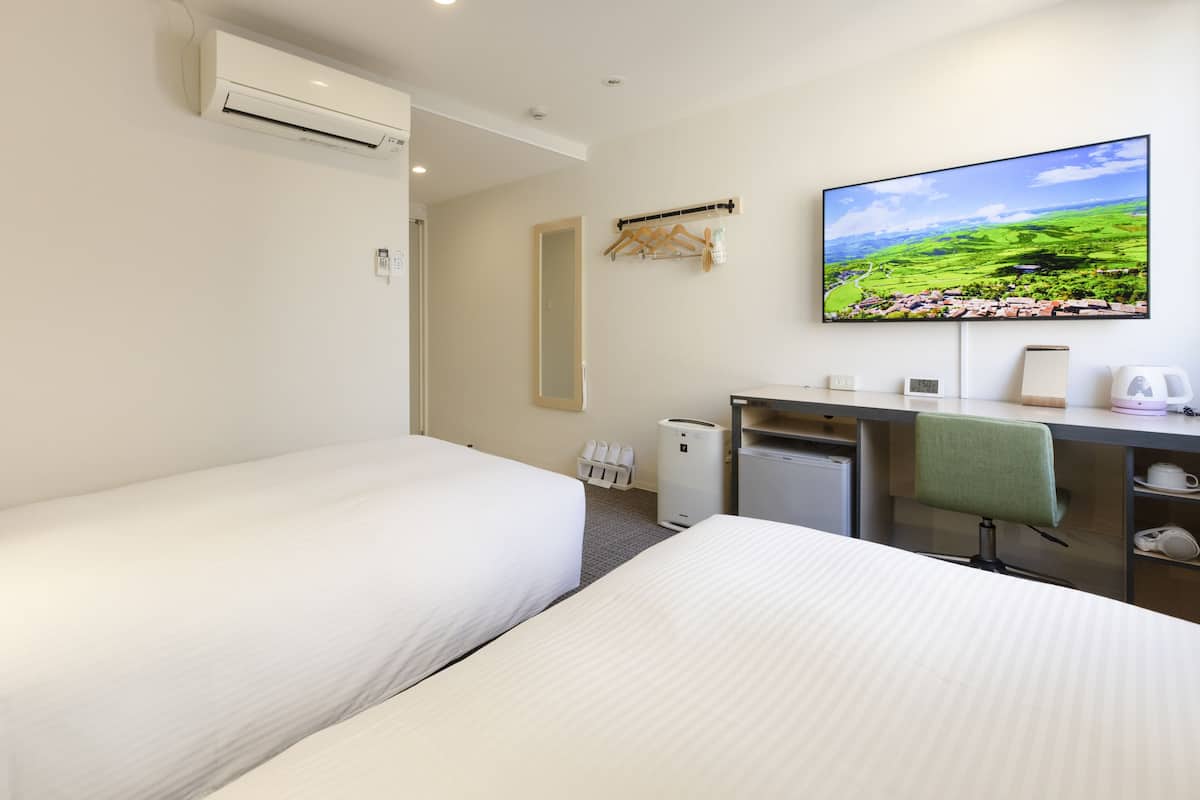 Ein Hotelzimmer mit zwei Betten, einem Schreibtisch, einem Sessel, einem Fernseher und Blick auf eine grüne Landschaft.