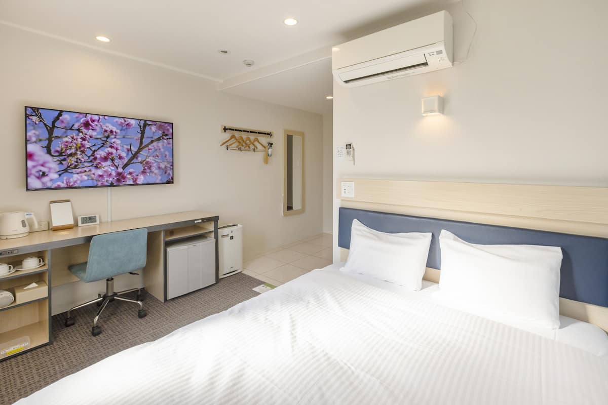 Ein Hotelzimmer mit Bett, Schreibtisch, Stuhl und einem Fernseher, der ein Blumenbild zeigt.
