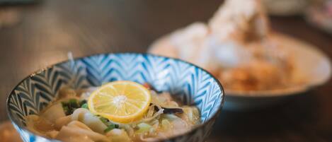 A bowl of soup with a lemon slice on top, placed on a wooden table.