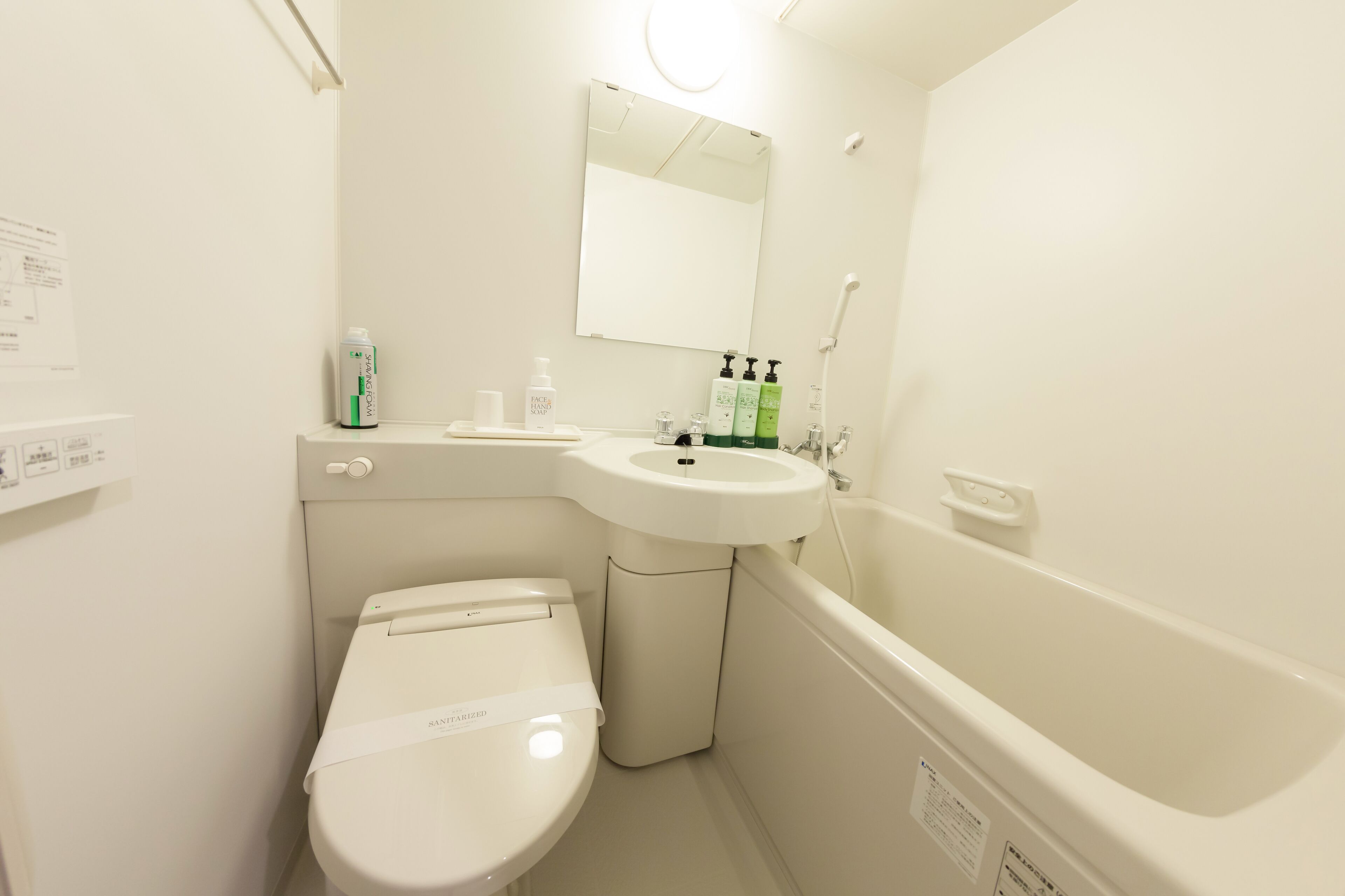 A small, white bathroom with a toilet, sink, and bathtub. There are toiletries on the sink counter.