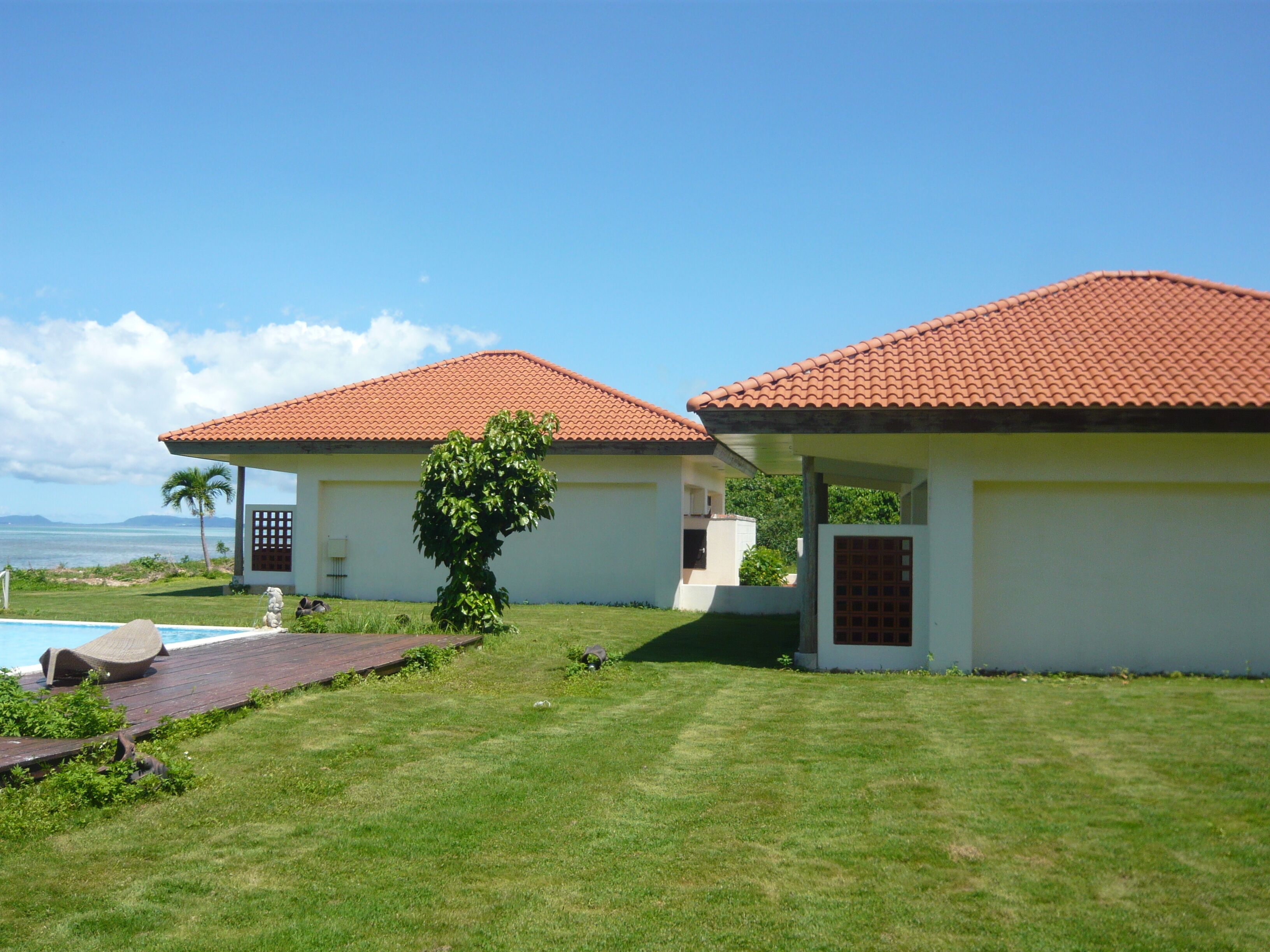 A two-story house with a red-tiled roof, a swimming pool, and a view of the ocean.