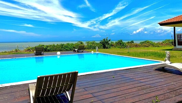 A clear blue sky with a wooden deck, a swimming pool, and a view of the ocean. - Eco Village Iriomote (Taketomi)