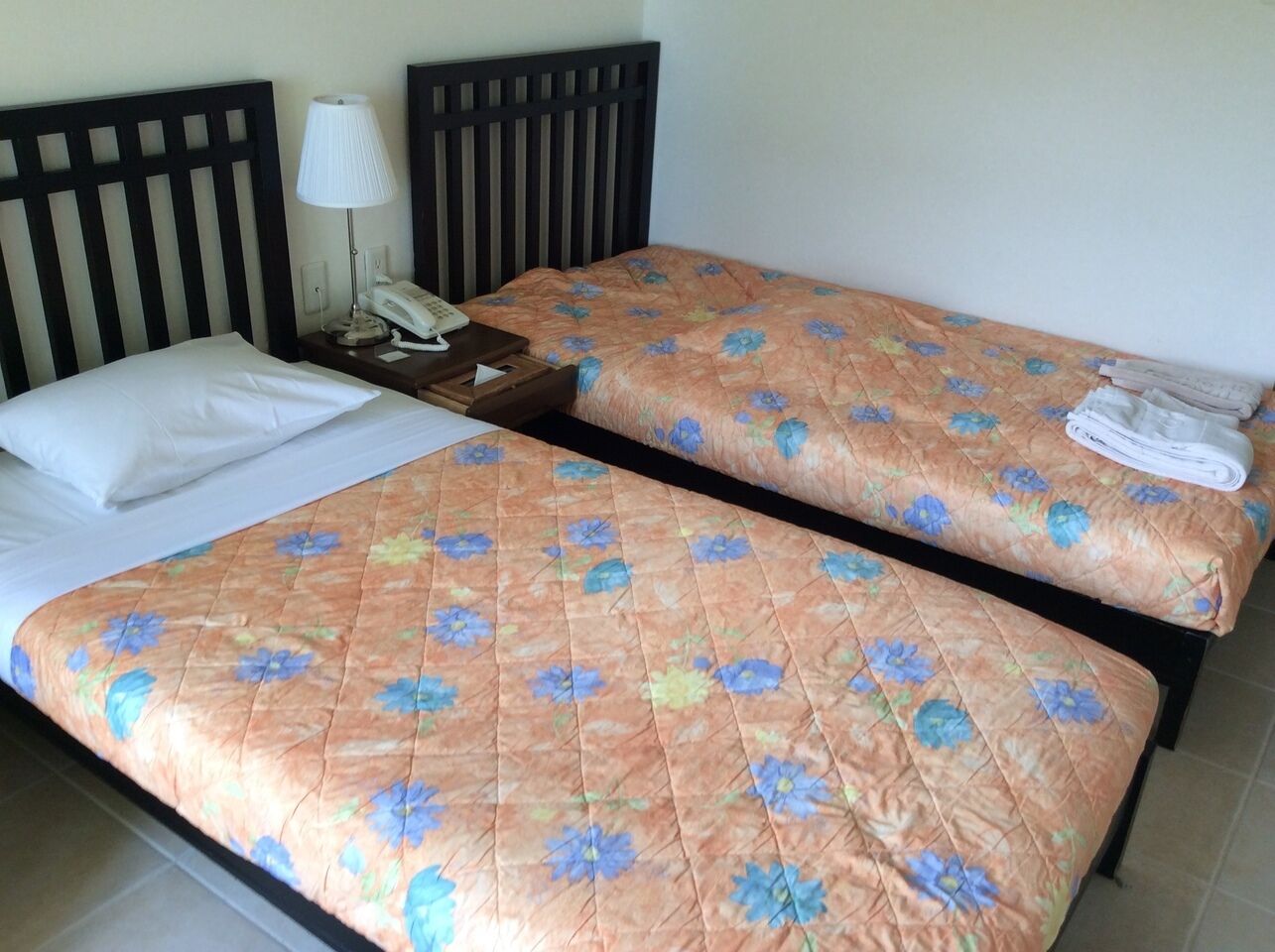 Un letto matrimoniale con copripiumino floreale, una lampada da comodino e un asciugamano piegato a destra.