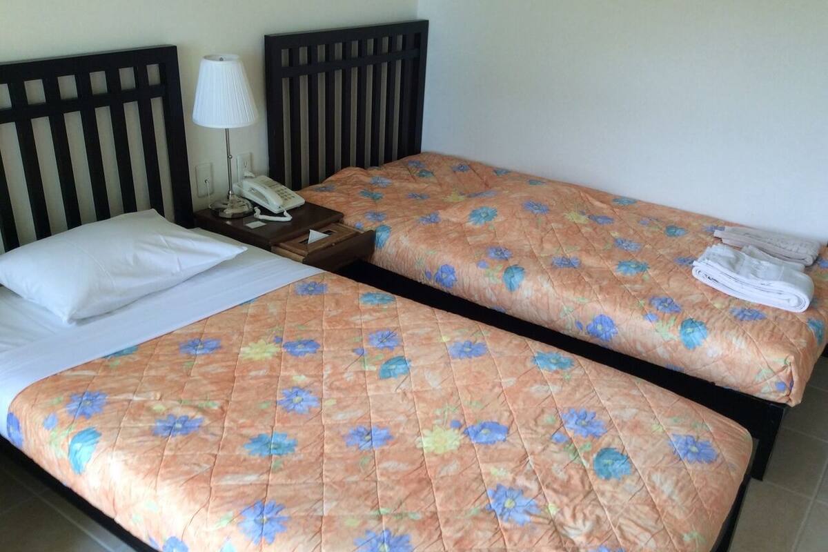 Un letto matrimoniale con copripiumino floreale, una lampada da comodino e un asciugamano piegato a destra.