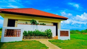 A two-story house with a red-tiled roof, white exterior walls, and a stone foundation. - Eco Village Iriomote (Taketomi)