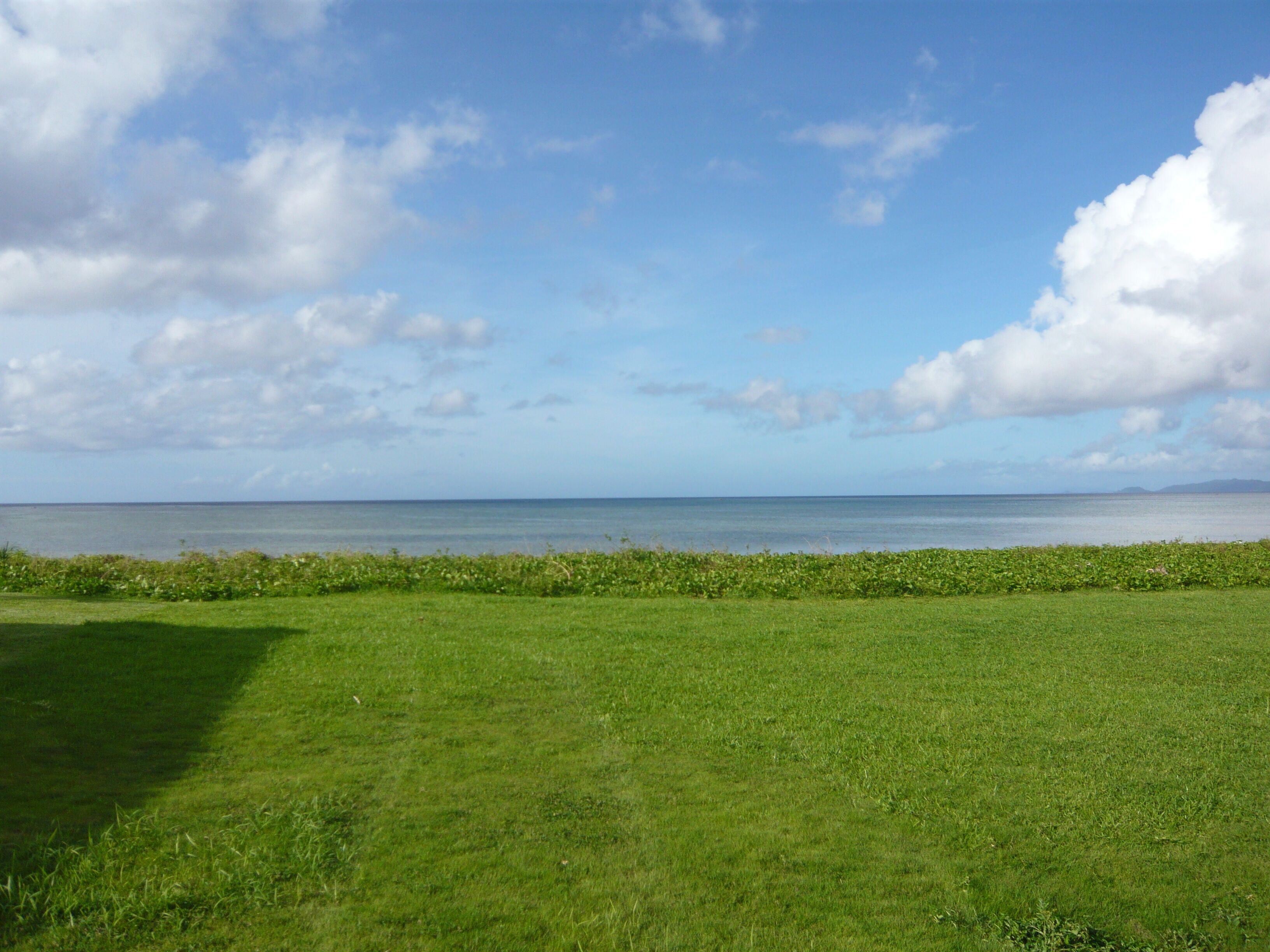 A grassy field with a view of the sea and distant land.