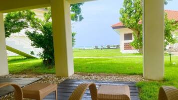 A covered outdoor seating area with wicker furniture, a view of a grassy lawn, and a building in the background.