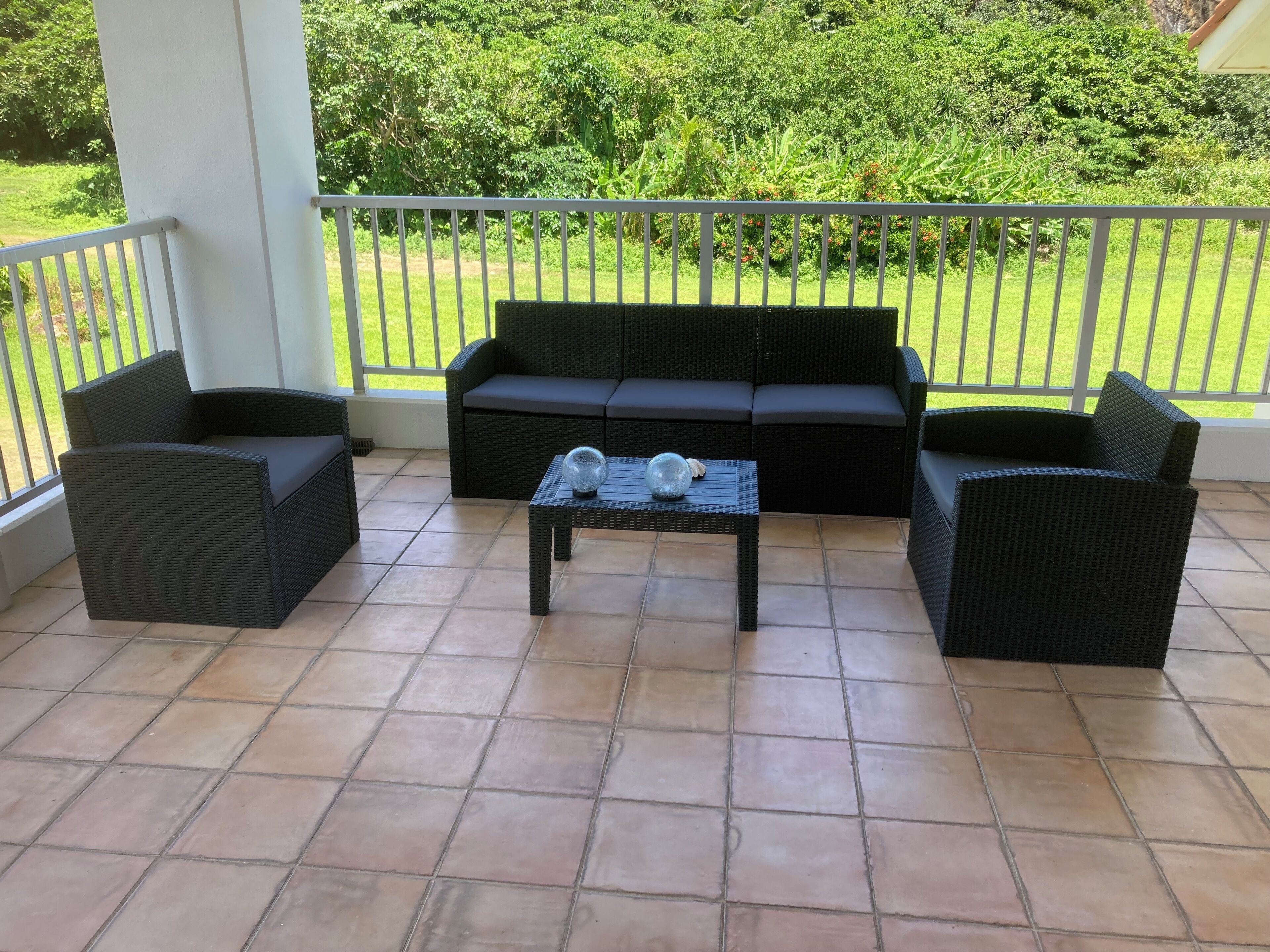 A covered patio area with a black wicker sofa set, two armchairs, and a small table with decorative items.