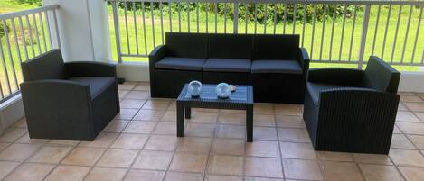 A covered patio area with a black wicker sofa set, two armchairs, and a small table with decorative items.