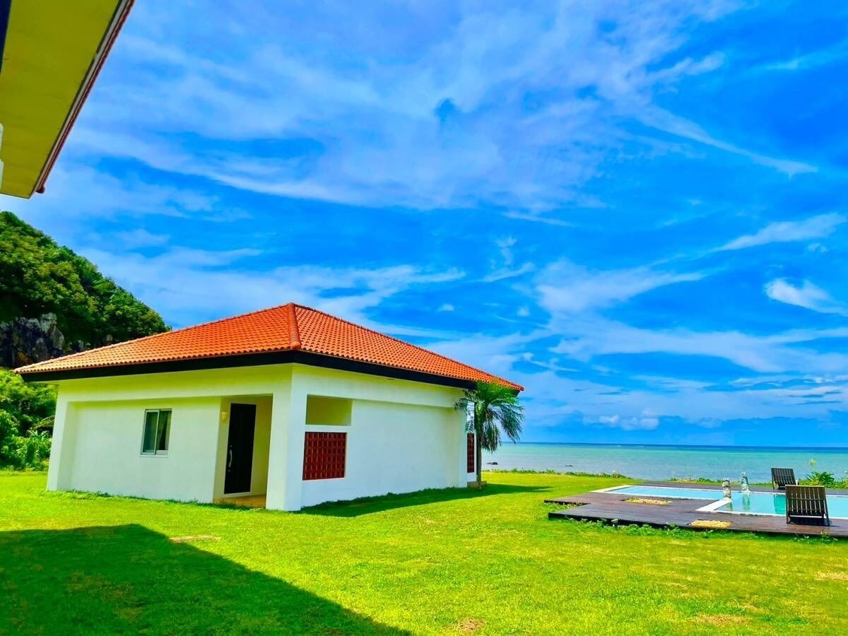 Un piccolo edificio bianco con tetto rosso, una piscina e vista sull'oceano.