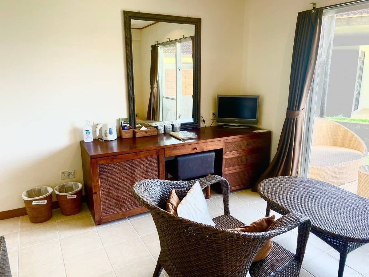 A room with a wooden desk, a television, wicker furniture, and a large mirror.