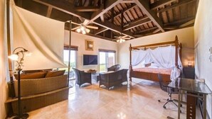 A spacious room with a large bed, a desk, and a chair. There is a ceiling fan, a window, and a lamp. - Eco Village Iriomote (Taketomi)
