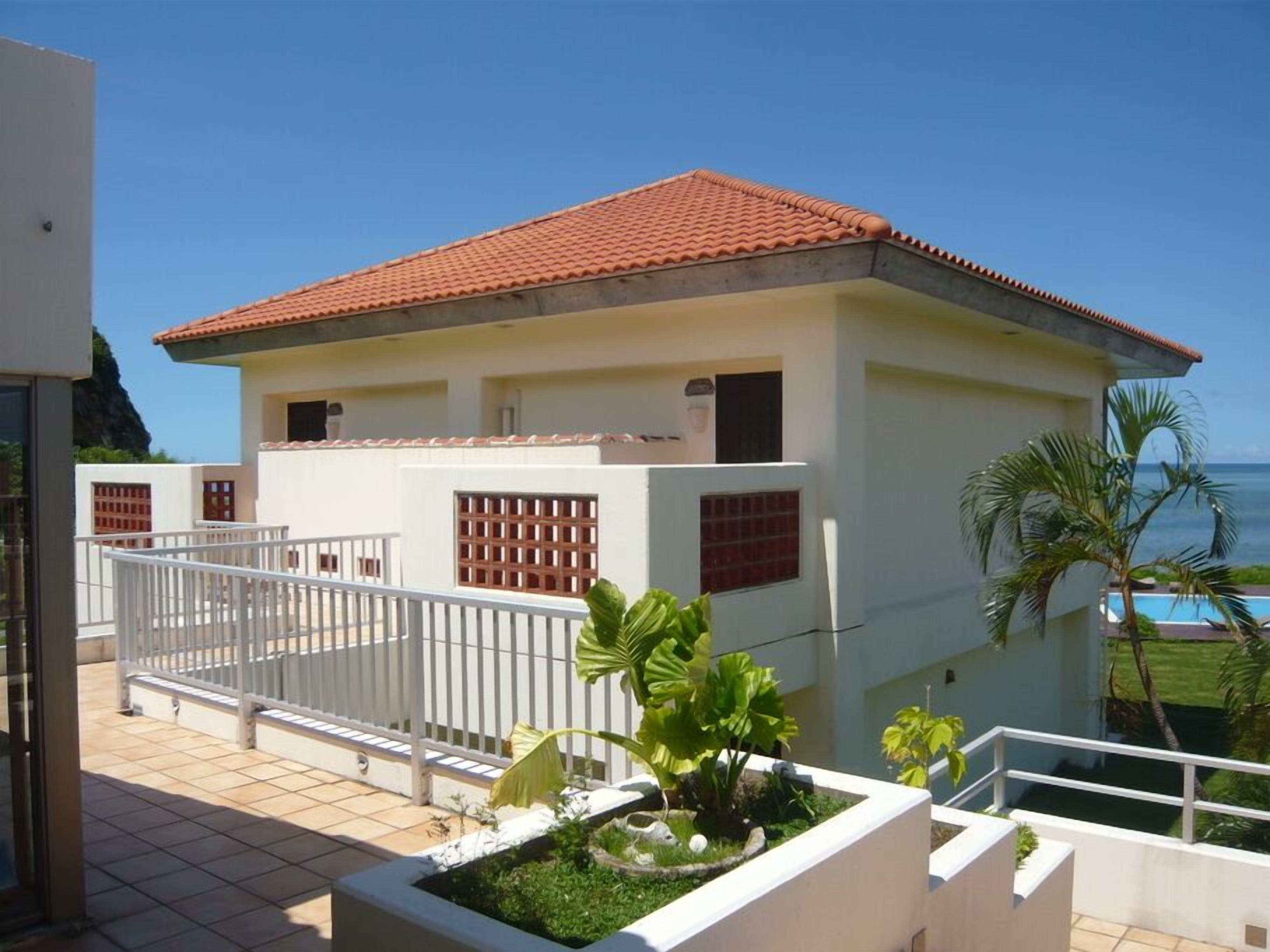 Un edificio a due piani con tetto in tegole rosse, pareti bianche e un balcone con ringhiera bianca.