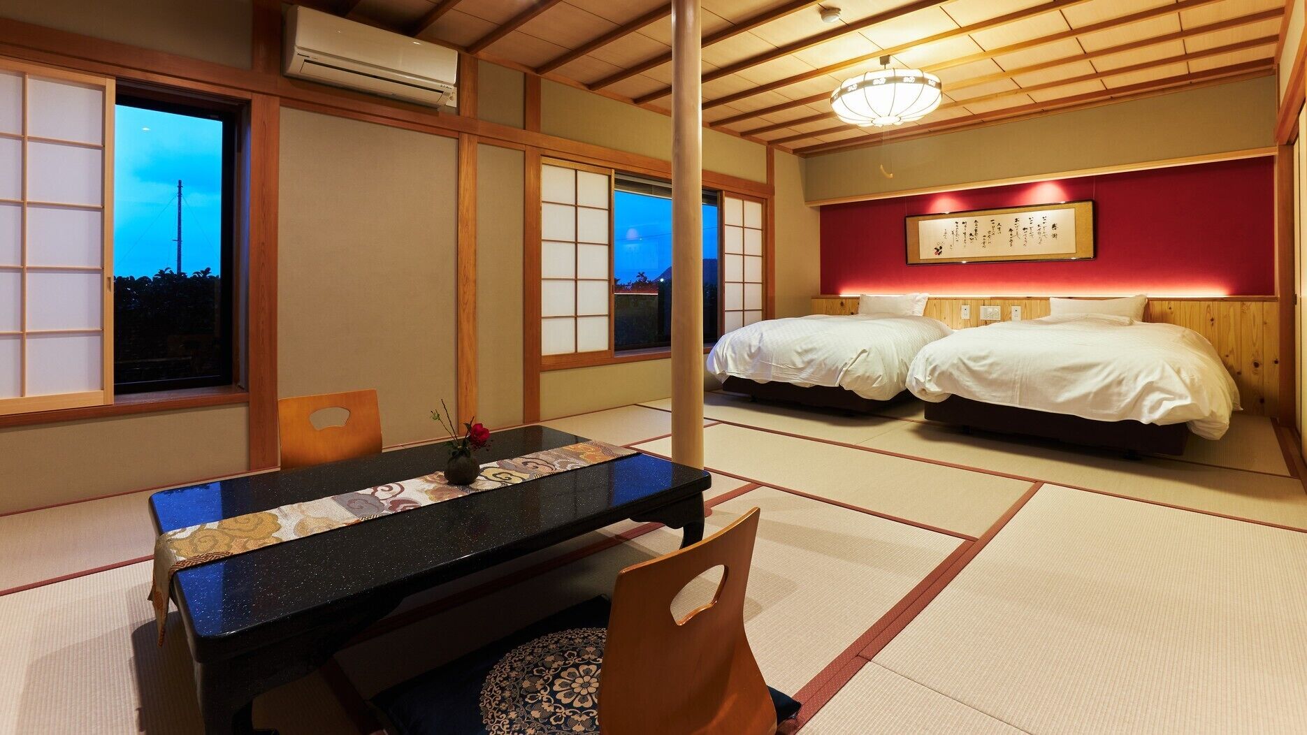 A traditional Japanese room with tatami flooring, a low table, two beds, and a wall-mounted air conditioner.