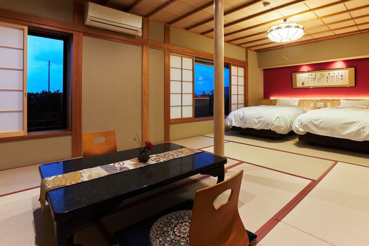 A traditional Japanese room with tatami flooring, a low table, two beds, and a wall-mounted air conditioner.