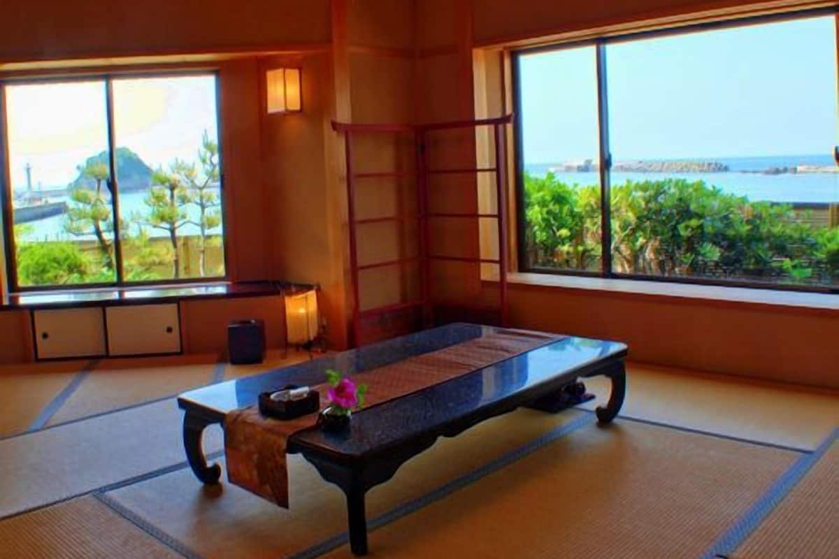 A tatami mat room with a low table, a ladder, and a view of the sea.
