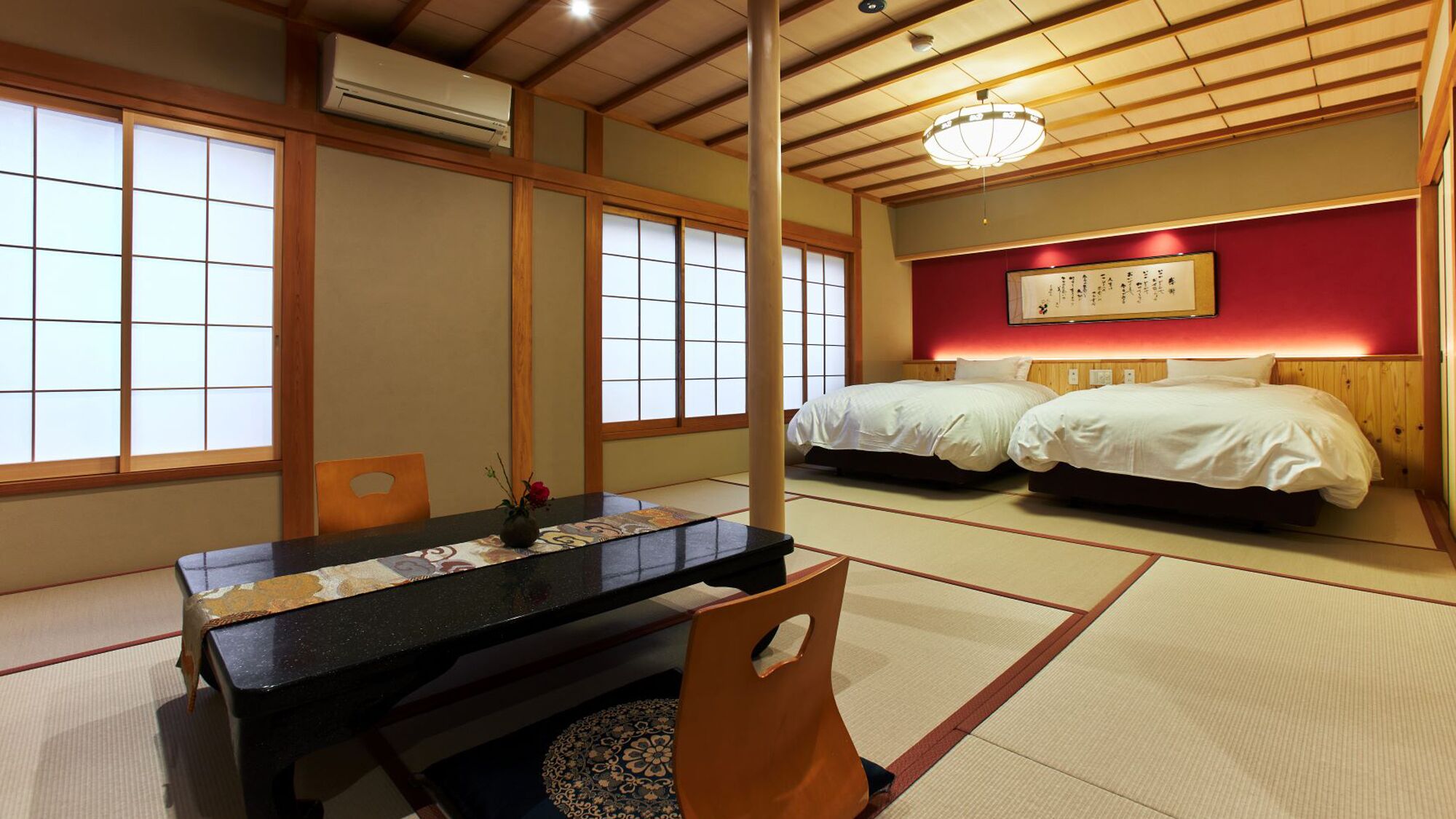 A traditional Japanese room with tatami flooring, a low table, two beds, and a ceiling fan.