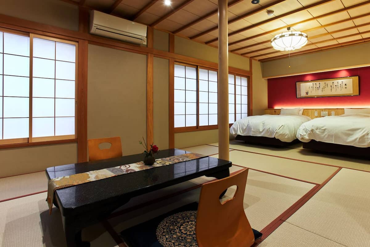 A traditional Japanese room with tatami flooring, a low table, two beds, and a ceiling fan.