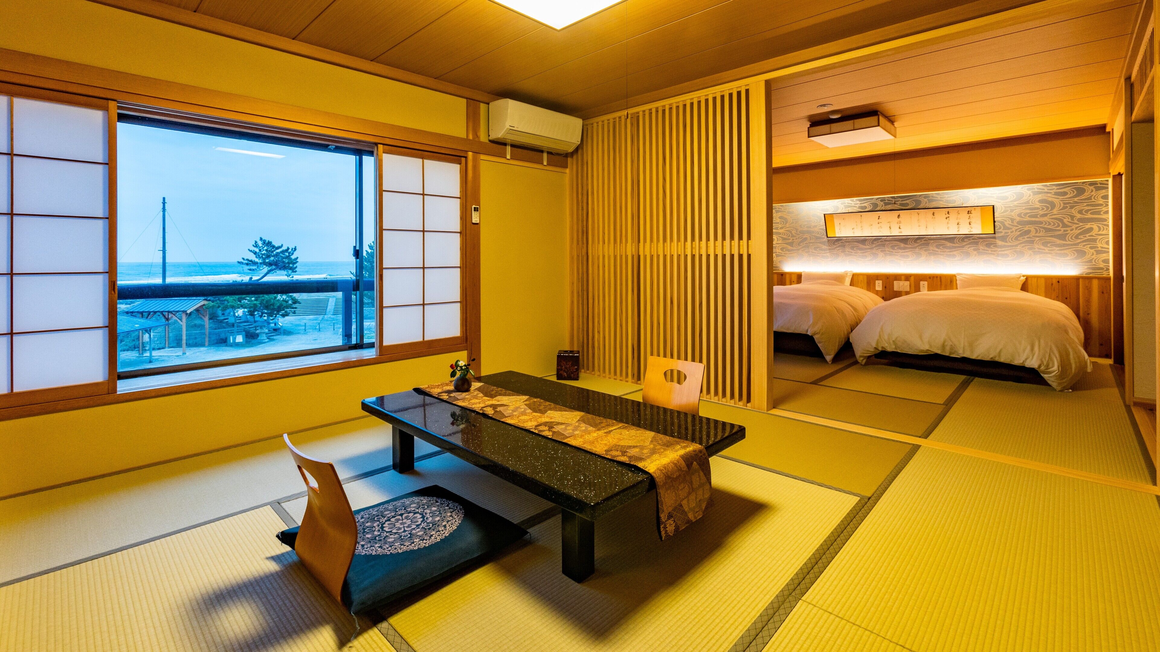 A traditional Japanese room with tatami flooring, a low table with a cushion, a futon bed, and a view of the sea through shoji screens.