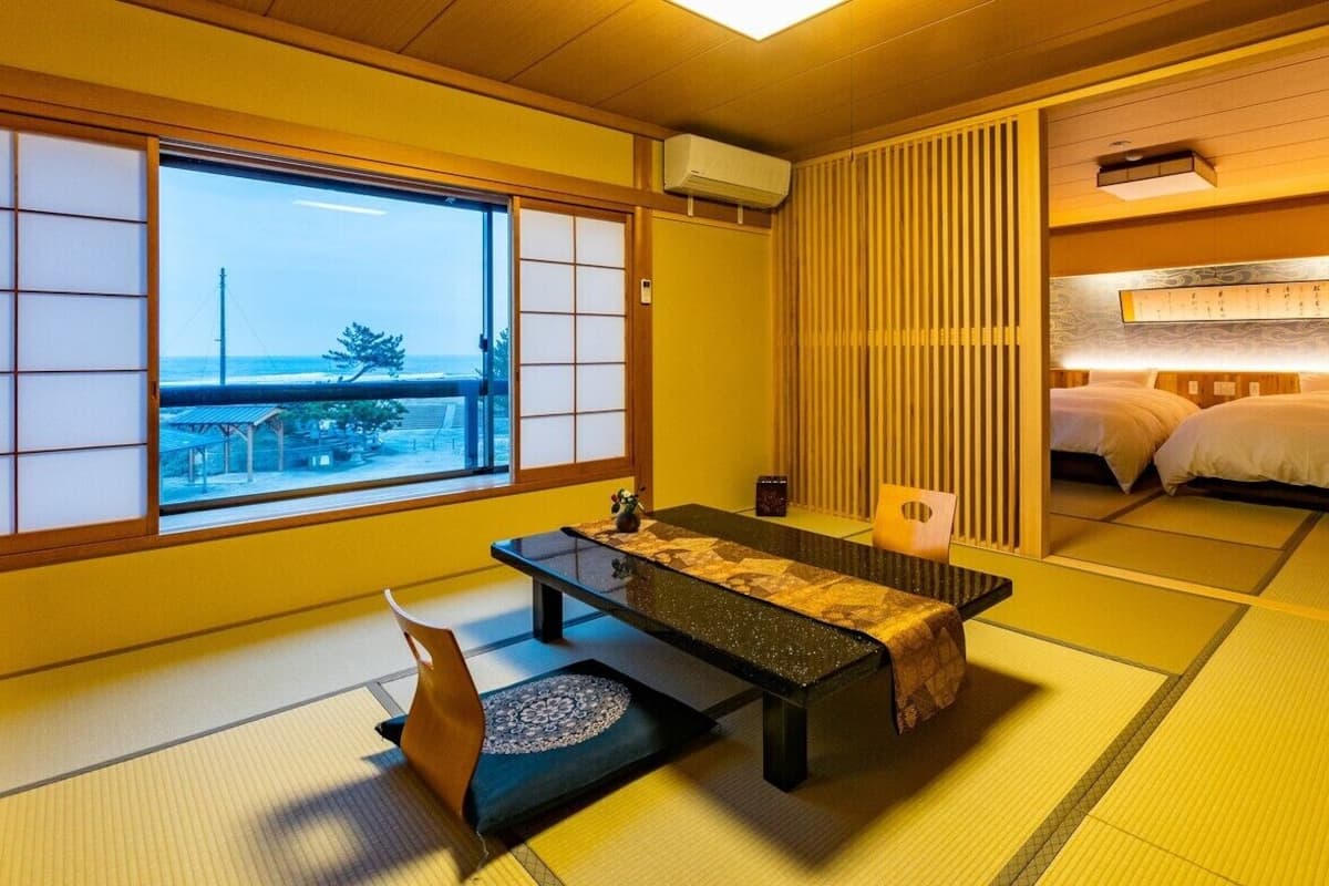A traditional Japanese room with tatami flooring, a low table, a futon bed, and a view of the sea.