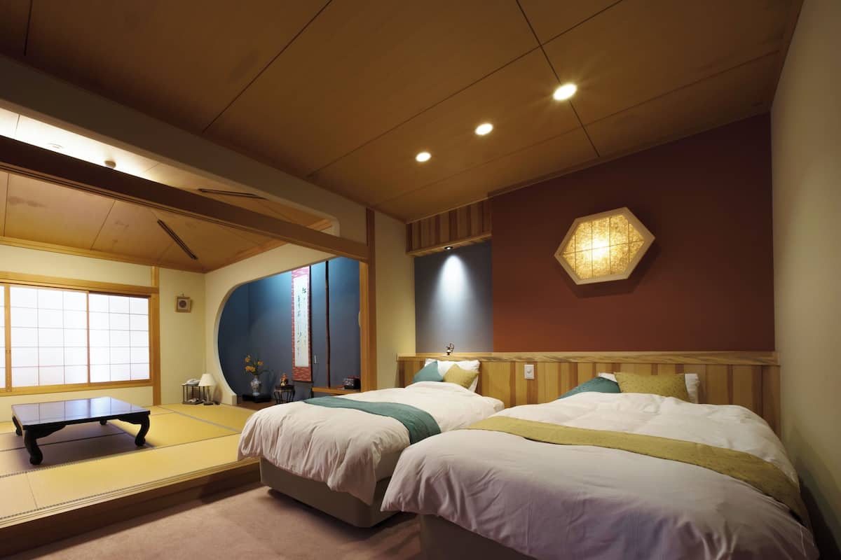 A room with two beds, a tatami mat, a small table, and a traditional Japanese-style window.