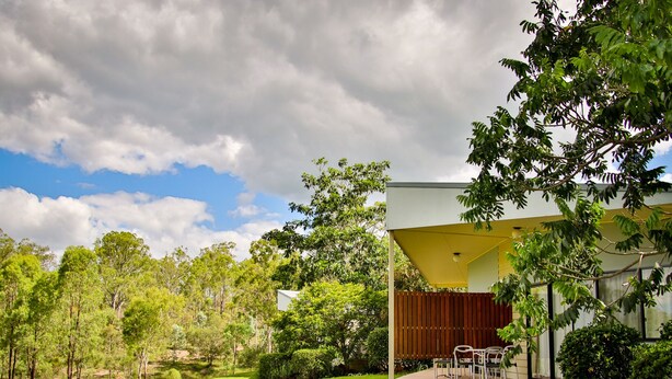 Une maison moderne dotée d’un espace extérieur aménagé et abrité, entourée d’une végétation luxuriante et d’arbres.