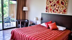 Une chambre d’hôtel avec un grand lit, une vue sur l’extérieur, un coin repas et un tableau au mur.