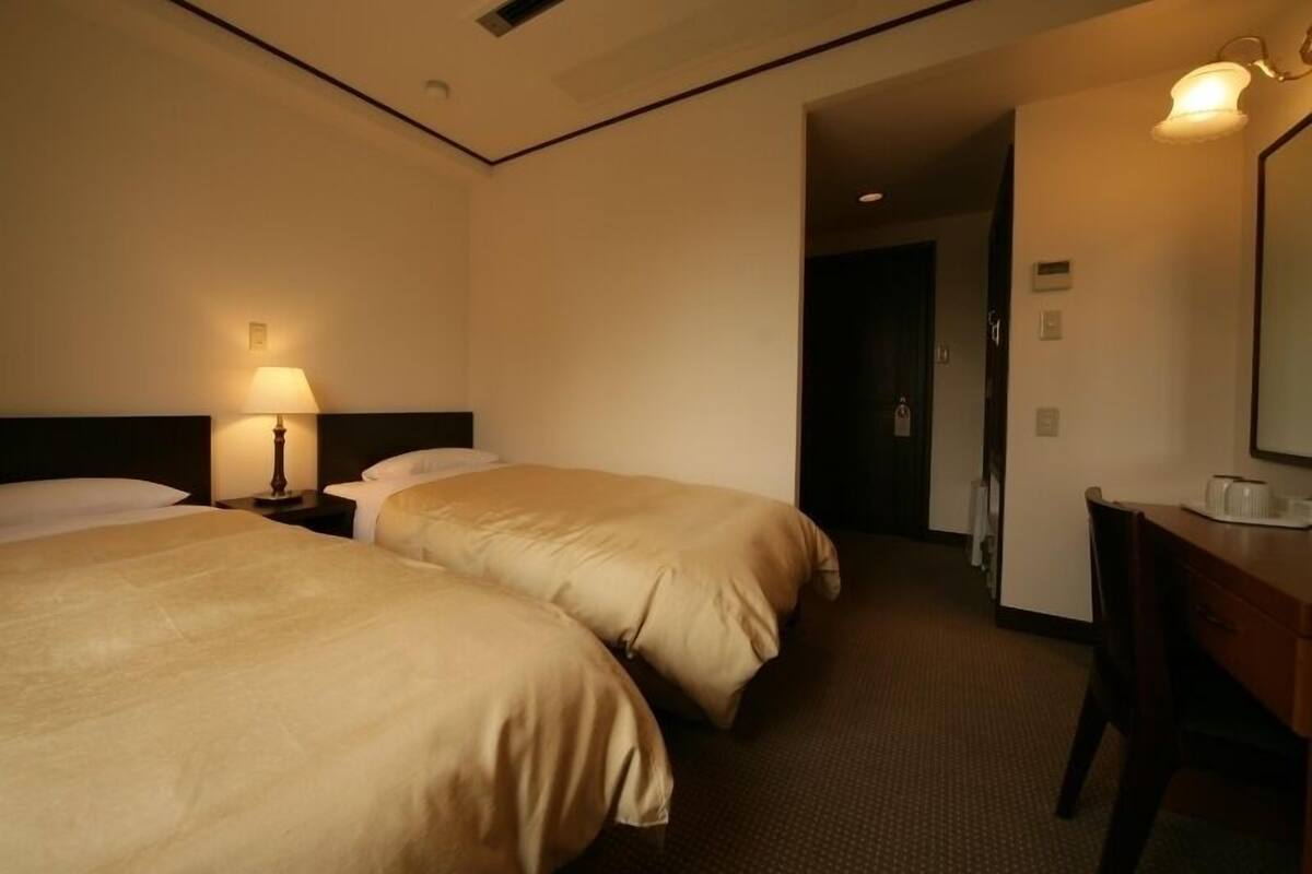 Habitación de hotel con dos camas, un escritorio, un espejo y una puerta que da a otra habitación.