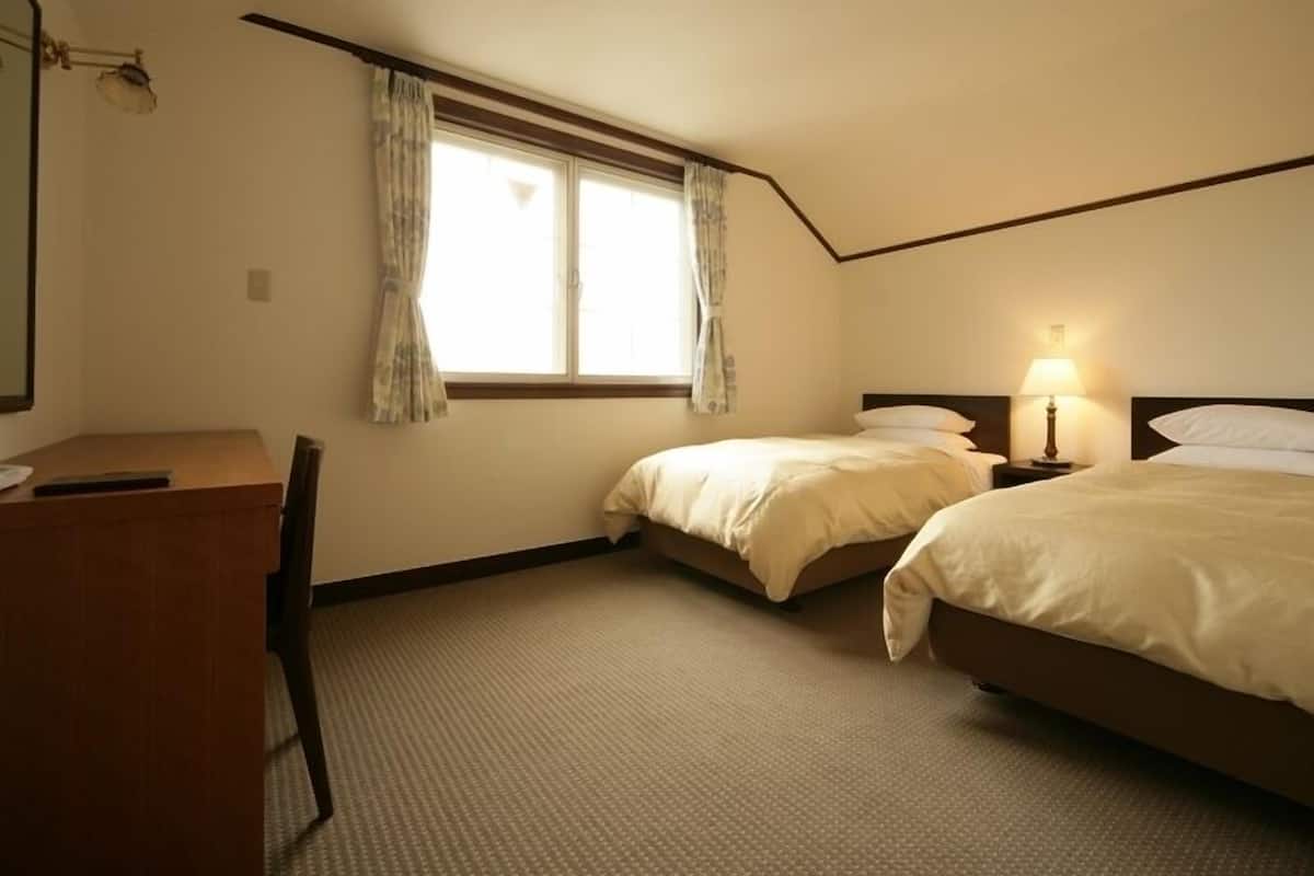 Habitación de hotel con dos camas, un escritorio, una lámpara y una ventana con cortinas.