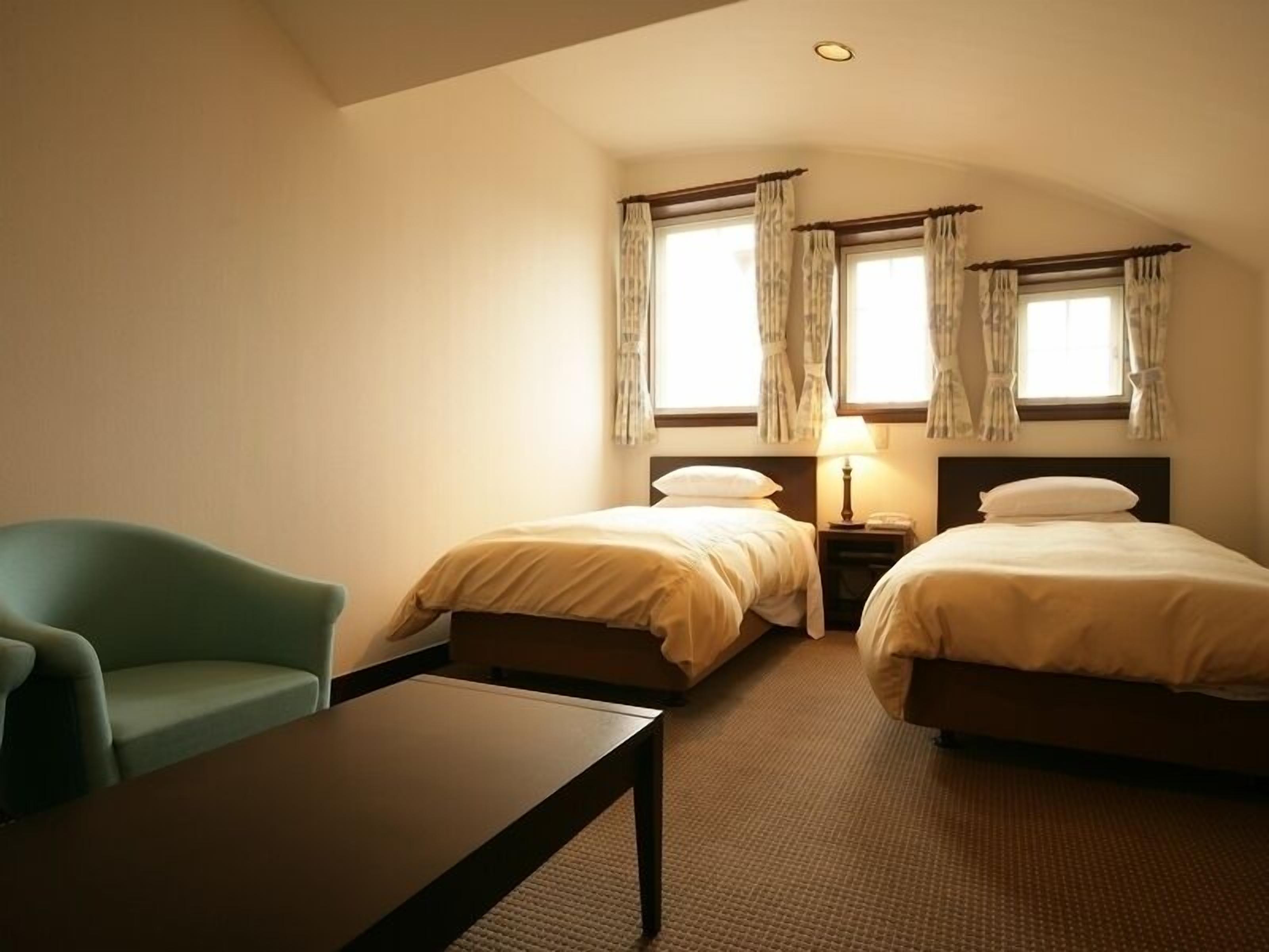 A hotel room with two beds, a desk, a chair, and a window with curtains.