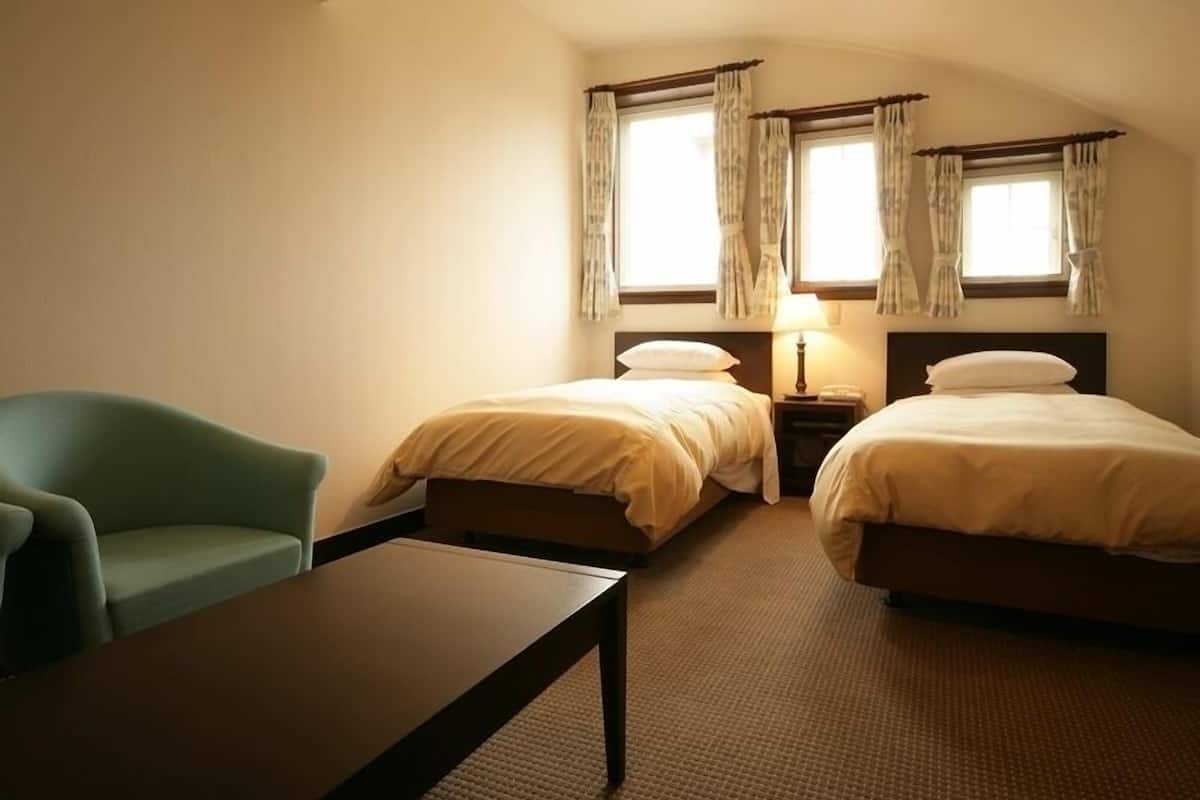 Habitación de hotel con dos camas, un escritorio, una silla y una ventana con cortinas.
