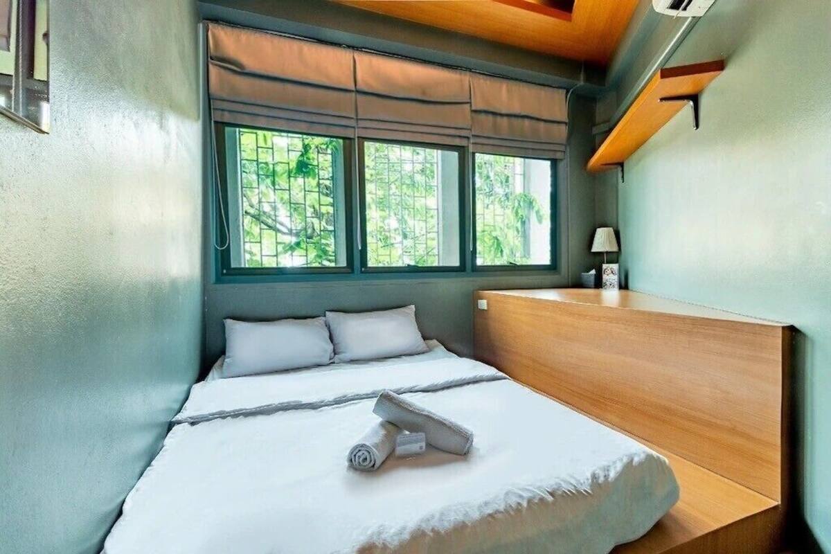 Una cama individual con cabecera de madera, una ventana con vistas a vegetación y una mesita de noche con lámpara.