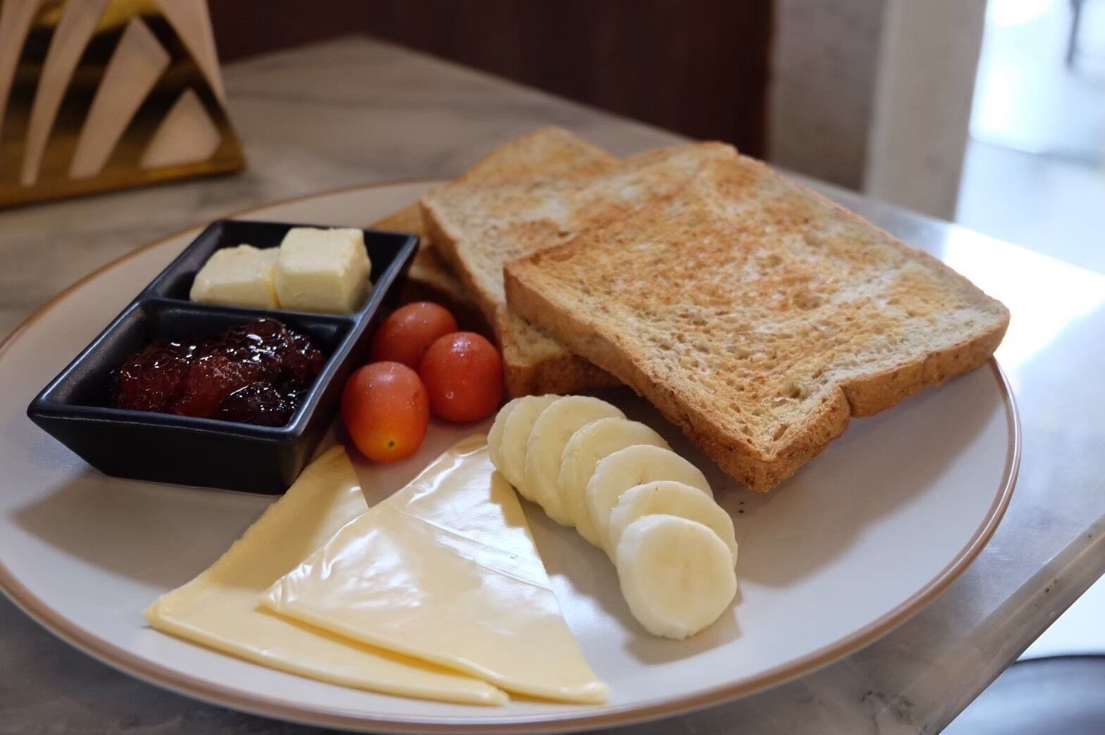 A plate with slices of bread, cheese, tomatoes, and a small container of jam.