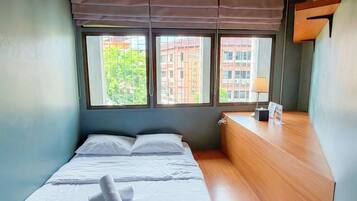 A bedroom with a bed, a wooden dresser, a lamp, and a window with a view of buildings.