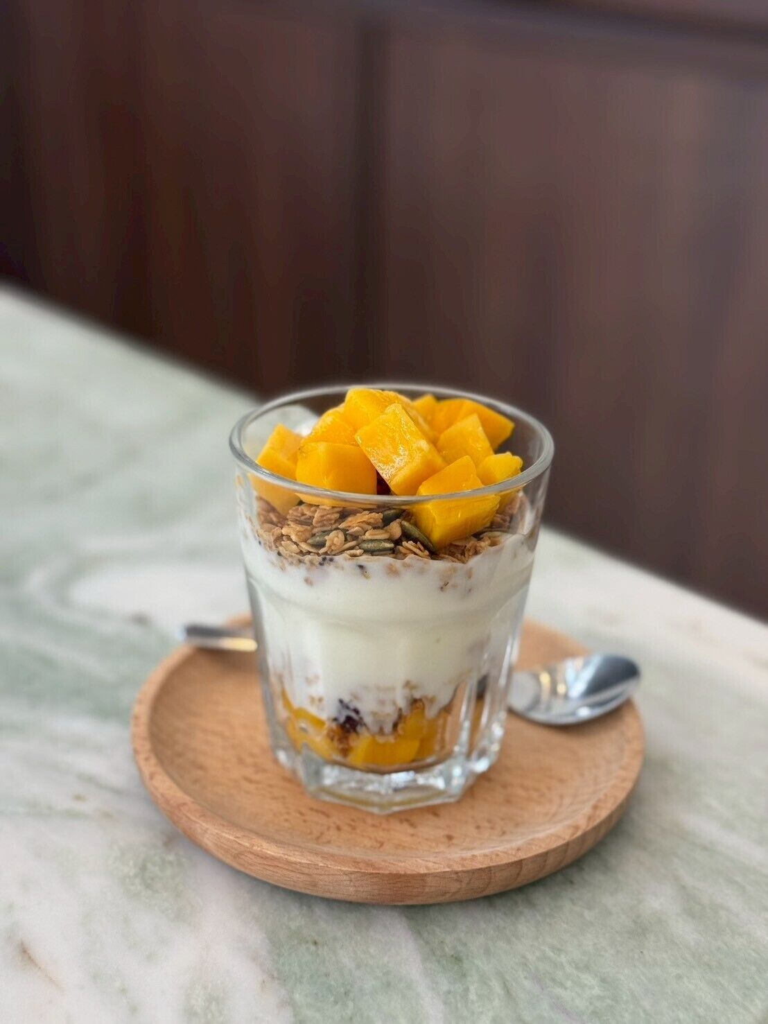 Ein mehrschichtiges Dessert in einem Glas auf einem Holzuntersetzer.