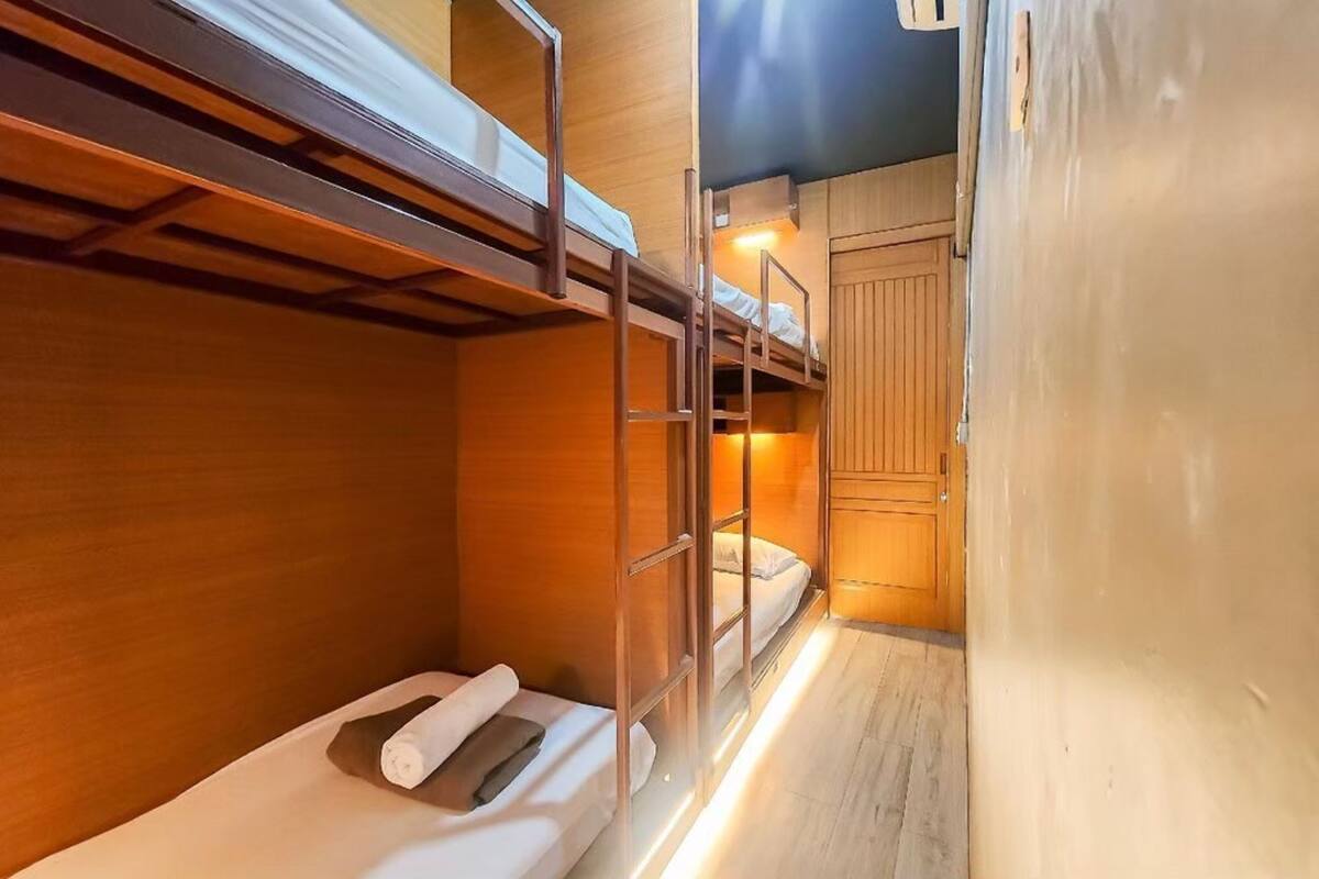 Habitación con literas, paredes de madera, un armario pequeño y una cama individual con una toalla enrollada.
