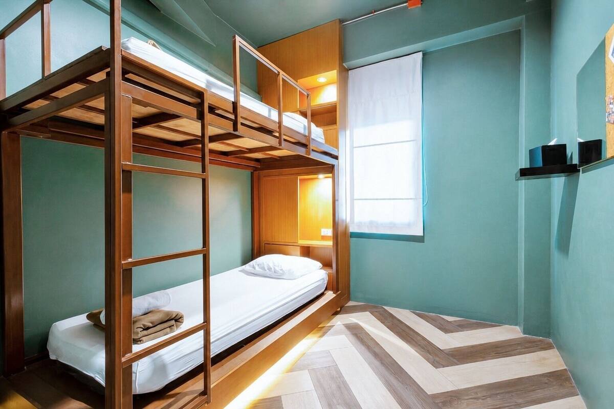 Habitación con literas, una escalera de madera, una cama individual, una mesita de noche, una lámpara y una ventana con cortinas.