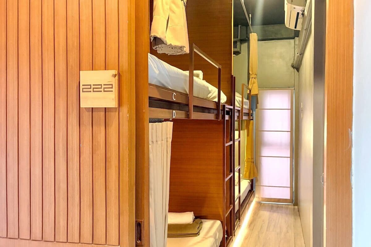 Un estrecho pasillo con literas, paneles de madera y un letrero con el número de habitación visible.