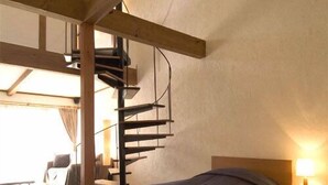 Une chambre avec deux lits, un escalier en colimaçon et une vue sur l’extérieur.