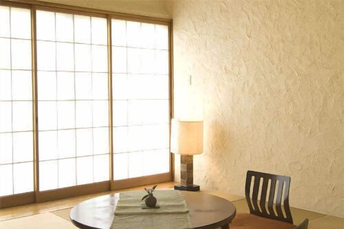 Una habitación con esterillas de tatami, una mesa redonda, dos sillas, una lámpara y vistas a través de biombos shoji.