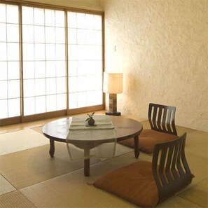 Ein Raum mit Tatami-Matten, einem runden Tisch, zwei Stühlen, einer Lampe und Blick durch Shoji-Schirme.